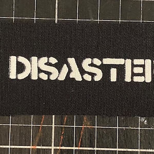 May include: A black fabric patch with the word "DISASTER" printed in white.