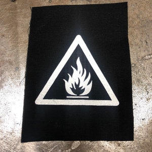 May include: A black fabric patch with a white triangle warning sign. The sign has a white flame symbol inside.