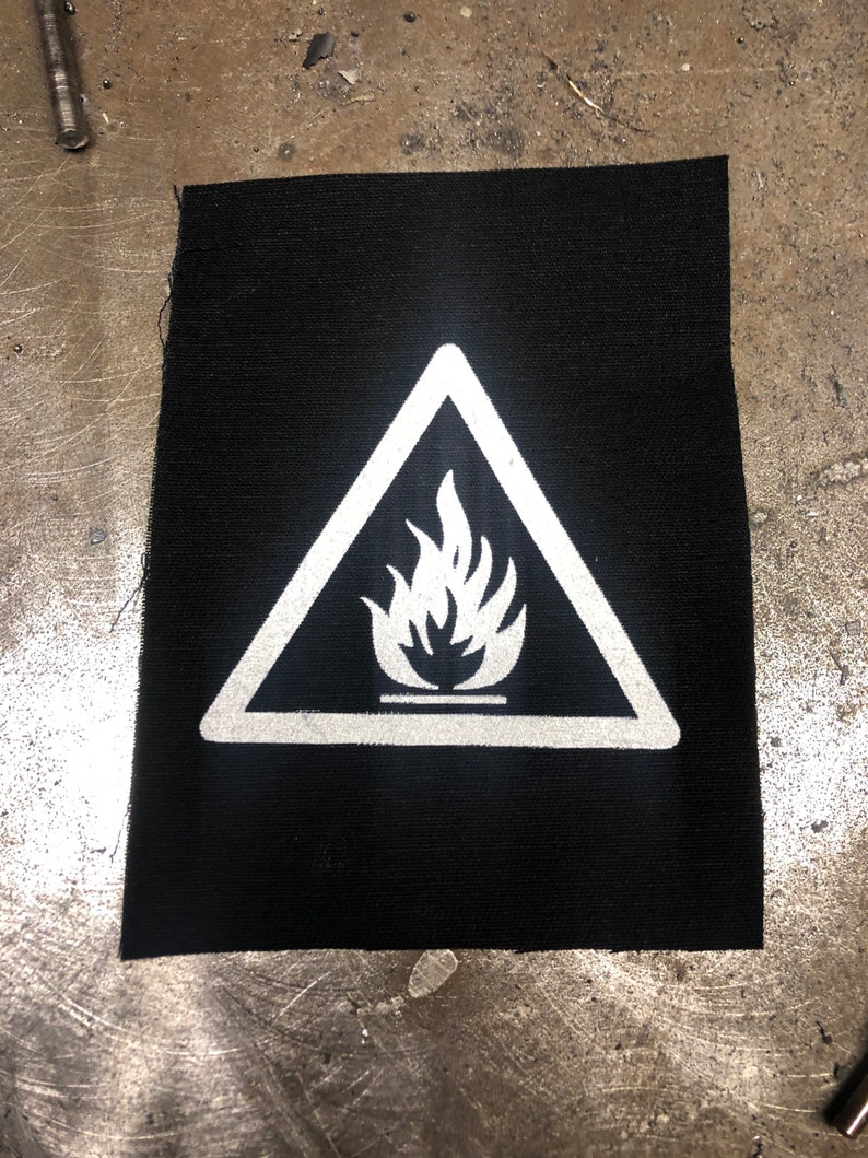May include: A black fabric patch with a white triangle warning sign. The sign has a white flame symbol inside.