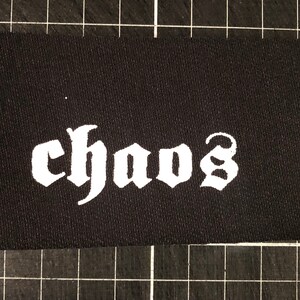 Peut inclure: Patch en tissu noir avec le mot "chaos" écrit en blanc dans une police gothique.