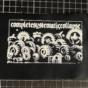 Könnte beinhalten: Schwarzer Stoffaufnäher mit dem weißen Schriftzug "completesystematiccollapse" in gotischer Schrift über einer detaillierten Illustration von ineinandergreifenden Zahnrädern. Der Aufnäher hat einen rohen Rand.