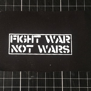 Könnte beinhalten: Schwarzer Stoff-Patch mit weißem Text, der "FIGHT WAR NOT WARS" in einem Rechteck zeigt.