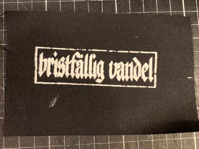 K&ouml;nnte beinhalten: Schwarzer Stoff-Patch mit wei&szlig;em Text, der "bristf&auml;llig vandel!" in einer gotischen Schriftart lautet.