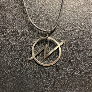 Può includere: Una collana d'argento con un ciondolo che presenta un fulmine stilizzato all'interno di un cerchio con una freccia che punta a destra.