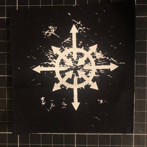 May include: Black square patch with a white eight-pointed star design with arrows. The symbol has a distressed, textured look. The patch is likely for clothing or accessories.