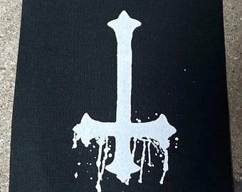 Puede incluir: Parche de tela negro con una cruz invertida blanca y gotas de pintura.