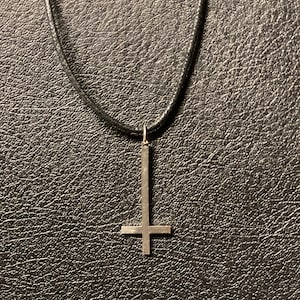 May include: A black leather cord necklace with a silver upside-down cross pendant.