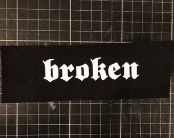 以下が含まれることがあります： 黒い布のパッチに、白いゴシック体で「broken」という単語が書かれています。