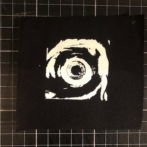May include: White eye patch with a swirling design on a black background. The eye patch is made of fabric and has a rough texture.