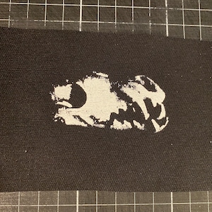 May include: White printed skull design on a black fabric patch.