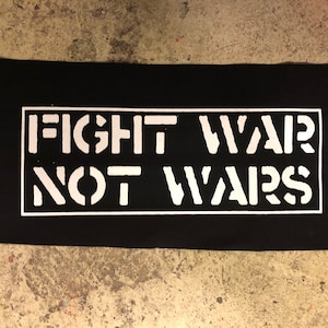 Puede incluir: Parche de tela negro con texto blanco que dice "FIGHT WAR NOT WARS" en un cuadro rectangular.