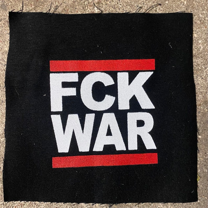May include: Square black patch with the words "FCK WAR" in large white letters. A red horizontal stripe is above and below the text. The patch is made of fabric.