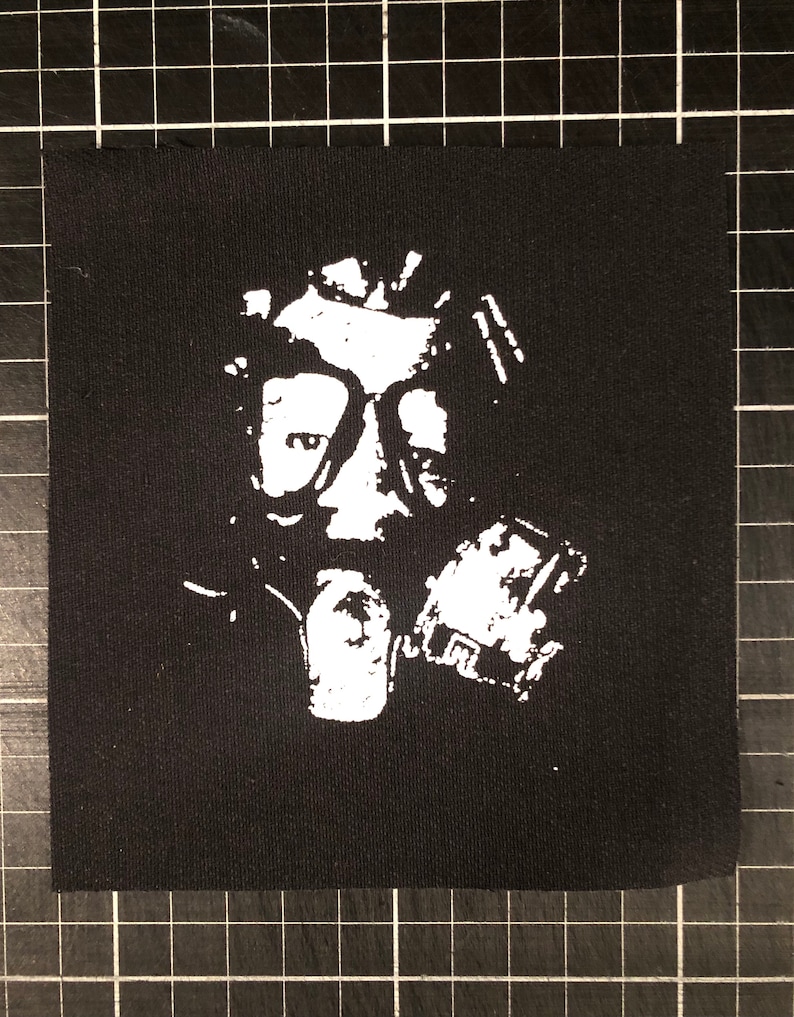 May include: A black and white patch featuring a person wearing a gas mask. The image is a silhouette with a white outline.