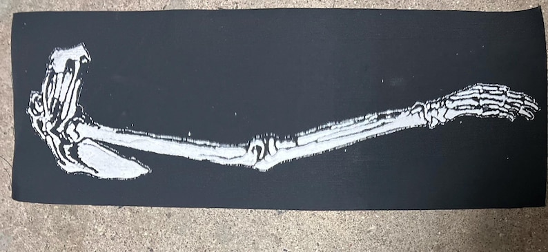 K&ouml;nnte beinhalten: Ein schwarzes rechteckiges Design mit einem wei&szlig;en Skelettarms und einer Hand. Der Arm ist in einem detaillierten, anatomischen Stil dargestellt, mit sichtbaren Knochen und Gelenken. Das Design ist ein starker Kontrast von Schwarz und Wei&szlig;.