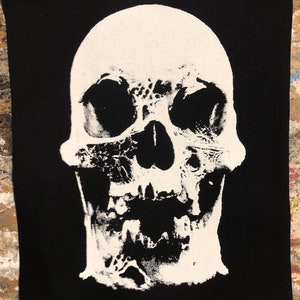 May include: A white skull with a detailed, textured design is printed on a black fabric patch.