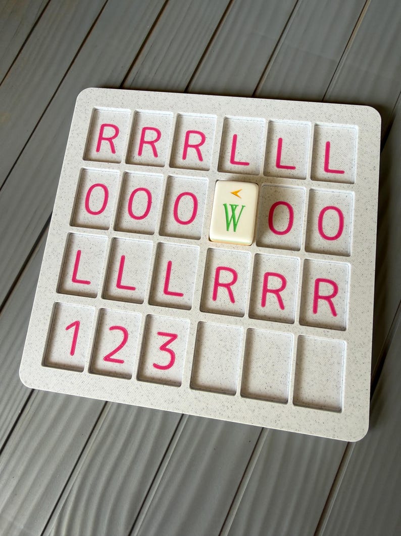 May include: A white speckled plastic grid board with four rows of rectangular slots. The slots contain pink printed letters R, L, O and numbers 1, 2, 3. A single cream-colored tile with a green letter W and a small orange arrow sits in one slot.