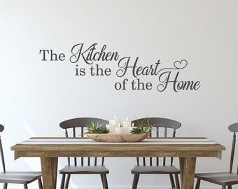 May include: A wooden dining table with four chairs and a decorative centrepiece. The wall behind the table has a vinyl decal that reads "The Kitchen is the Heart of the Home".