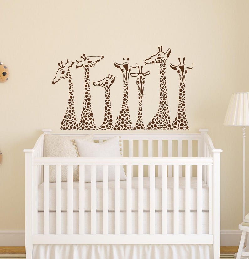 May include: A white crib with a brown giraffe decal on the wall above it. The decal features seven giraffes in a row, all facing the same direction. The giraffes are brown with a spotted pattern.