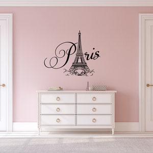 May include: A white dresser with six drawers and gold handles sits in front of a pink wall with a black Eiffel Tower and the word "Paris" in cursive.