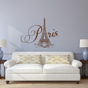 May include: A white couch with two pillows sits in front of a light blue wall with a brown Eiffel Tower and the word "Paris" in cursive.