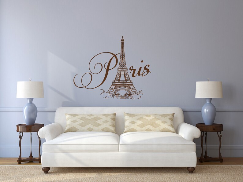 May include: A white couch with two pillows sits in front of a light blue wall with a brown Eiffel Tower and the word "Paris" in cursive.
