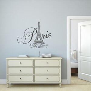May include: A white dresser with six drawers and black knobs. The dresser is in front of a light blue wall with a black and white Eiffel Tower and the word "Paris" in a cursive font.