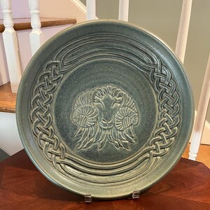 May include: A green ceramic plate with a Celtic knot design around the edge and a raised image of a ram's head in the center.