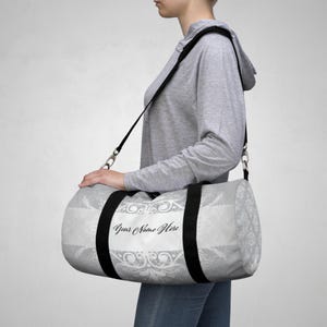 Könnte beinhalten: Eine weiße und graue Reisetasche mit schwarzem Trageriemen und weißem Blumenmuster. Die Tasche trägt den Text "Your Name Here".