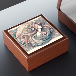 May include: A wooden box with a hinged lid. The lid features a colorful illustration of a woman with flowing hair and flowers. The box is a light brown color.