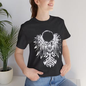 May include: A black t-shirt with a white graphic of a skull with wings. The skull is surrounded by a decorative floral design.
