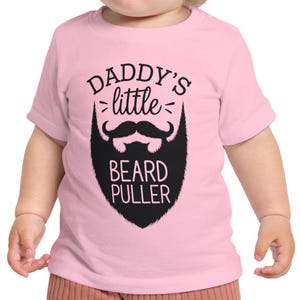 May include: Pink toddler t-shirt with black text that reads "Daddy's little beard puller" and a black cartoon beard with a mustache.