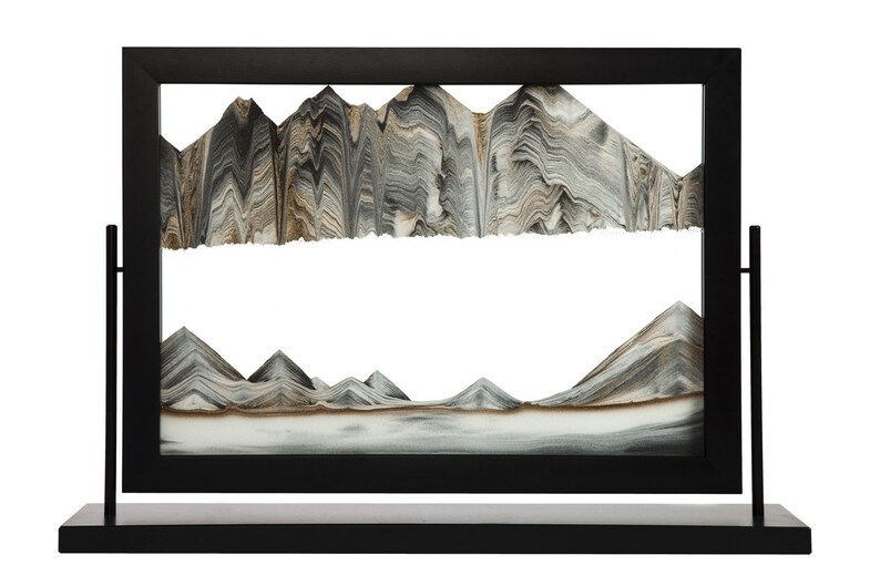 May include: A black sand art frame with a mountain scene. The sand is layered in shades of brown, gray, and white, creating a realistic mountain range.