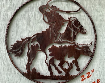 May include: A metal wall art sculpture depicting a cowboy riding a horse and roping a steer. The sculpture is 22 inches in diameter and has a rustic brown finish.