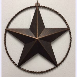 May include: A large, rustic, bronze-colored metal star with a rope-like wire frame. The star is hanging from a white wall.