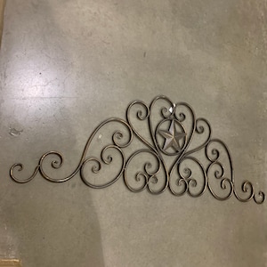 May include: A decorative metal wall hanging with a scrolled design and a five-pointed star in the center.