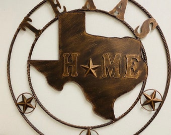 May include: A metal wall decor featuring the outline of the state of Texas with the word "HOME" inside. The state is surrounded by a rope-like circle with the word "TEXAS" written around it. There are four stars around the outer circle.