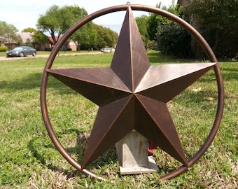 May include: A large, rustic, copper-coloured metal star with a circular frame. The star is mounted on a wooden post in a grassy yard.
