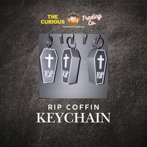 May include: Three gray coffin keyrings with white detailing, each featuring a cross and the letters "RIP". The keyrings hang from silver hoops. The text "RIP COFFIN KEYCHAIN" is displayed below the keyrings.