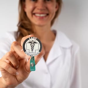 Peut inclure: Un porte-badge d'identification médicale blanc avec un badge rond noir et blanc qui dit "LAST RESPONDER" avec un symbole de caducée au centre.