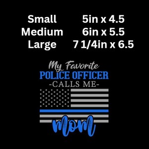 Puede incluir: Una camiseta negra con un dise&ntilde;o de bandera estadounidense azul y blanca con una fina l&iacute;nea azul. El texto "My Favorite Police Officer -Calls Me- mom" est&aacute; impreso en la camiseta. La camiseta est&aacute; disponible en tallas S, M y L. La S mide 5 pulgadas por 4,5 pulgadas, la M mide 6 pulgadas por 5,5 pulgadas y la L mide 7 1/4 pulgadas por 6,5 pulgadas.
