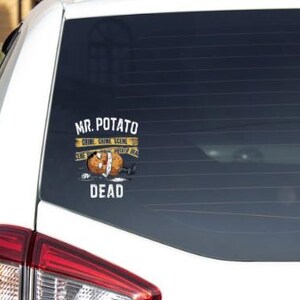 May include: A white car with a yellow and black sticker on the rear window that reads "Mr. Potato Crime Scene Potato Dead". The sticker depicts a cartoon potato with a bandage on its head and police tape around it.