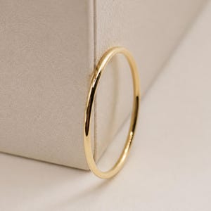 Puede incluir: Un anillo fino de oro amarillo pulido con una banda lisa y redondeada. El anillo presenta un dise&ntilde;o circular sencillo con una superficie met&aacute;lica reflectante que capta la luz, mostrando un aspecto limpio y uniforme en toda la banda.