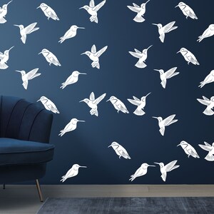 May include: A dark blue wall with a white hummingbird pattern. The hummingbirds are in various positions, some flying, some perched. There is a dark blue armchair in the foreground.