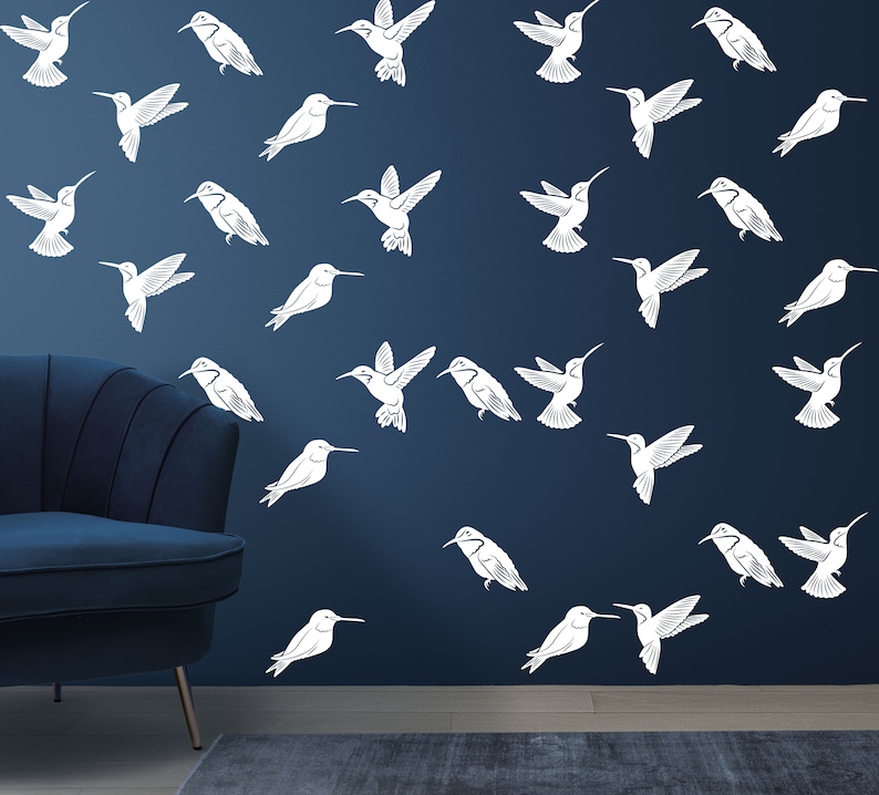 May include: A dark blue wall with a white hummingbird pattern. The hummingbirds are in various positions, some flying, some perched. There is a dark blue armchair in the foreground.