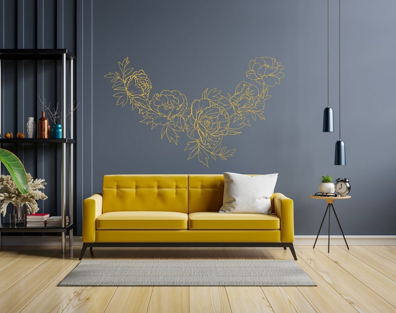 May include: A yellow velvet sofa with a white pillow sits in a living room with a dark gray wall and a gold floral design. The room has a black shelf with decorative items and a small table with a clock and a plant.