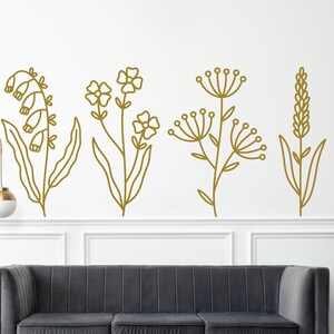 May include: Five gold outline floral designs on a white wall. The designs include a cluster of bell-shaped flowers, a cluster of small flowers, a cluster of small flowers with a larger flower at the top, a cluster of small flowers with a larger flower at the top, and a cluster of small flowers with a larger flower at the top.