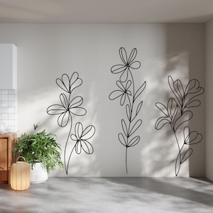 K&ouml;nnte beinhalten: Eine wei&szlig;e Wand mit drei schwarzen Linienzeichnungen von stilisierten Blumen. Die Blumen sind einfach und abstrakt, ohne Bl&auml;tter oder Stiele.
