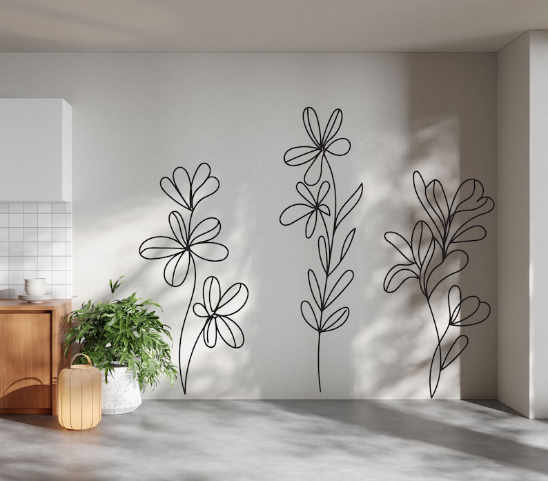 K&ouml;nnte beinhalten: Eine wei&szlig;e Wand mit drei schwarzen Linienzeichnungen von stilisierten Blumen. Die Blumen sind einfach und abstrakt, ohne Bl&auml;tter oder Stiele.