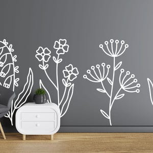 May include: White outline wall decals of various flowers and plants on a gray wall. The decals are in a row across the wall. There is a white nightstand with two drawers in the lower right corner of the image.