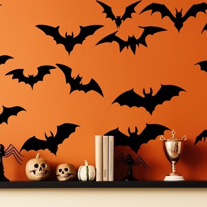 Może przedstawiać: Pomarańczowa ściana ozdobiona czarnymi sylwetkami nietoperzy o r&oacute;żnych rozmiarach. P&oacute;łka prezentuje dekoracje na Halloween, w tym rzeźbione dynie, czaszki i trofeum. Scena wywołuje świąteczną, upiorną atmosferę.